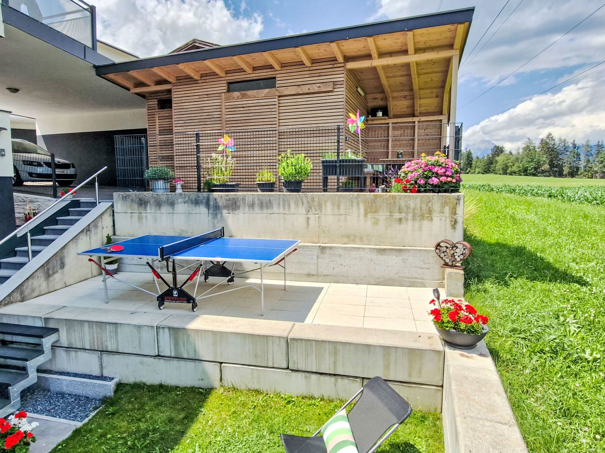 Ein moderner Außenbereich mit Tischtennisplatte, einer Treppe und einem Garten mit Blumentöpfen und Blumen.