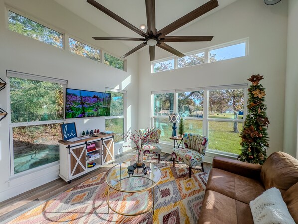 A spacious living room with a ceiling fan, large windows, a television, a coffee table, and a couch. - The Lake House, Pond, 3 Min to Lake, Pets Ok (Somerville)
