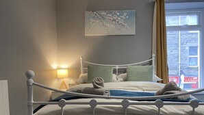 Un lit bien fait, avec une literie blanche et des coussins décoratifs, une lampe de chevet et un tableau représentant des fleurs de cerisier accroché au mur.