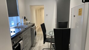 Une cuisine compacte équipée d’un évier, d’un lave-linge et d’un coin repas avec une table en verre et des chaises noires.