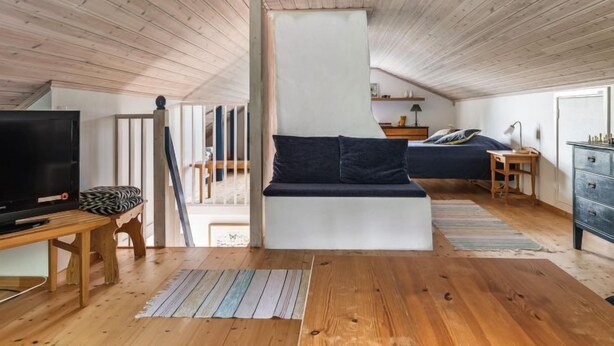A spacious loft bedroom with a high ceiling, wooden beams, a large bed, a TV, and a desk.