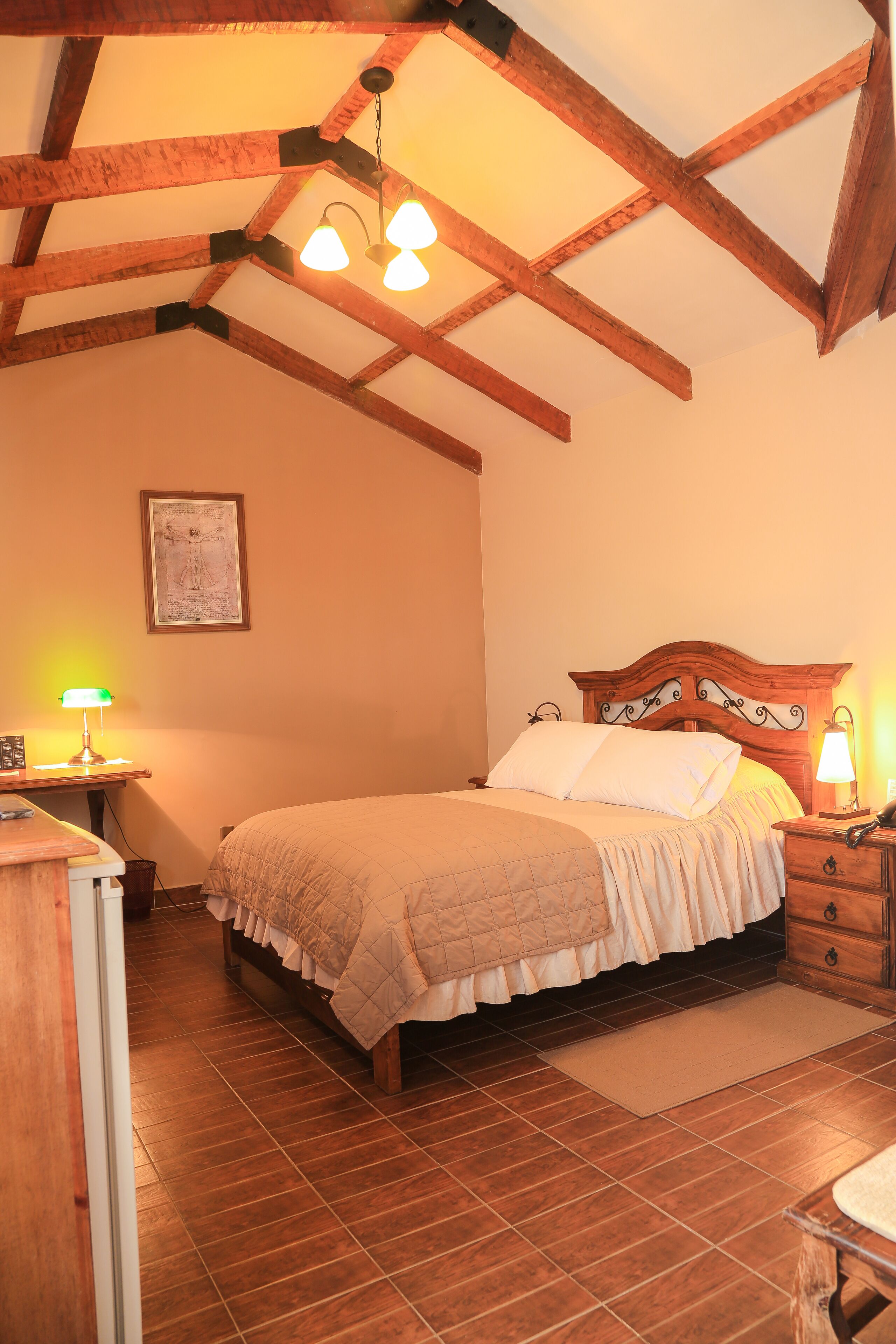 Un dormitorio con techo de madera, una cama con edredón blanco, una mesita de noche con lámpara y un cuadro en la pared.