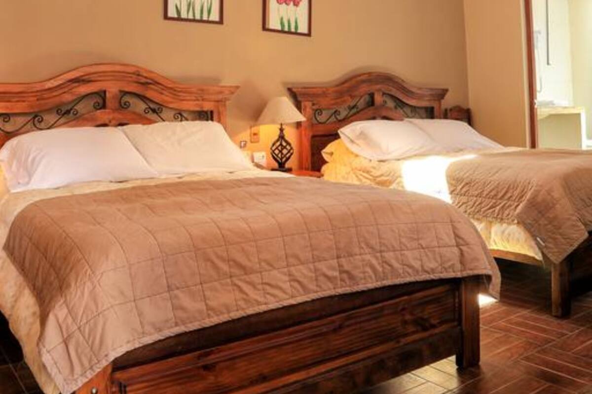 A room with two wooden beds, a sloped ceiling with exposed beams, and a chandelier.
