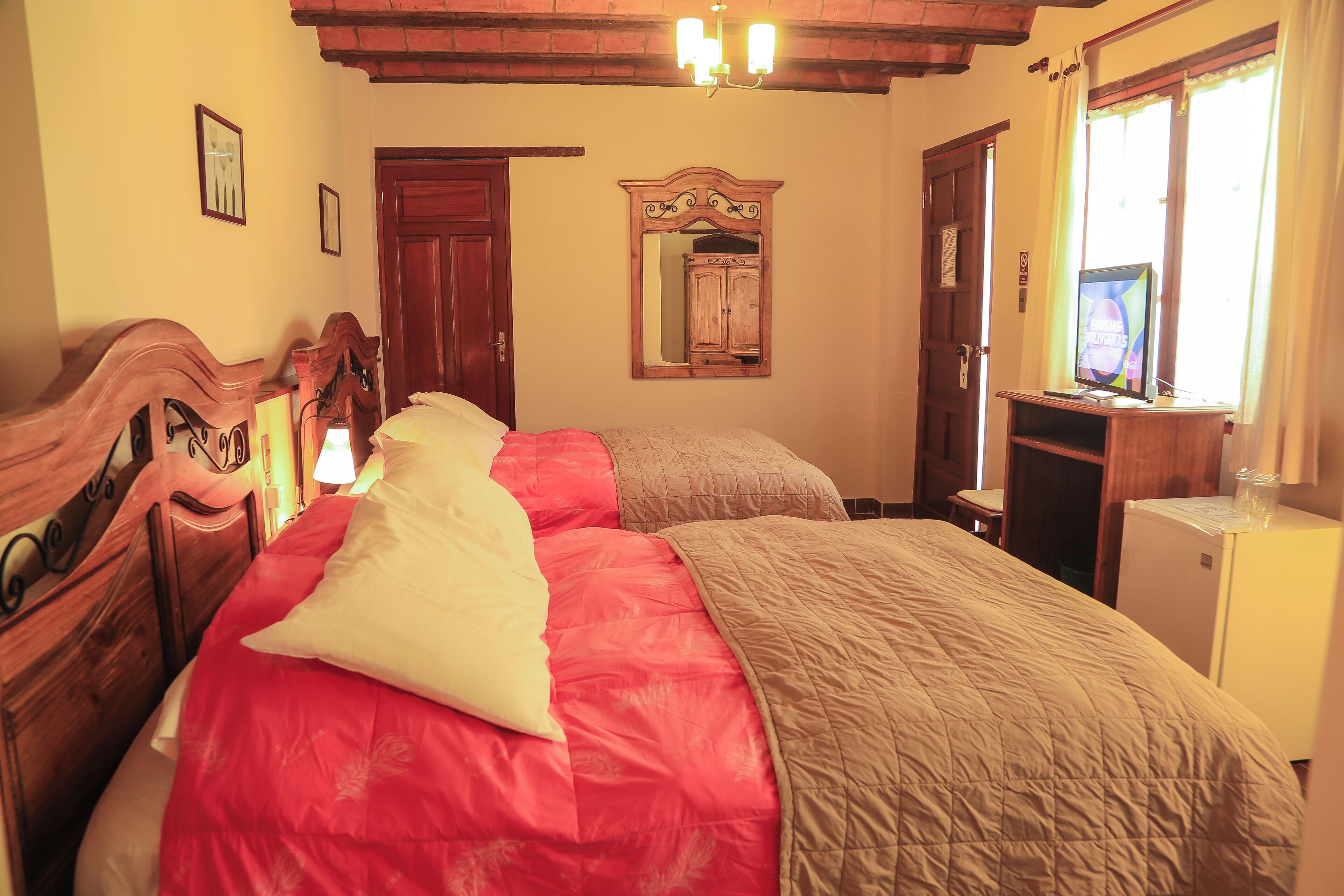 Un dormitorio con dos camas, cabeceros de madera, un espejo, un escritorio pequeño y una ventana con cortinas.