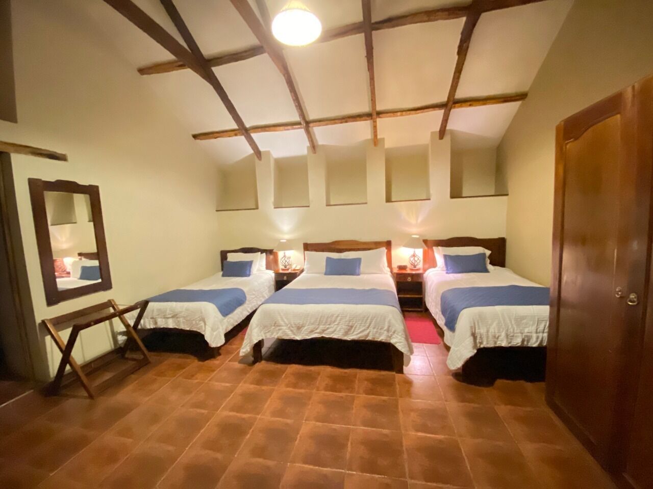 A room with three beds, a wooden ceiling, and a mirror on the left wall.