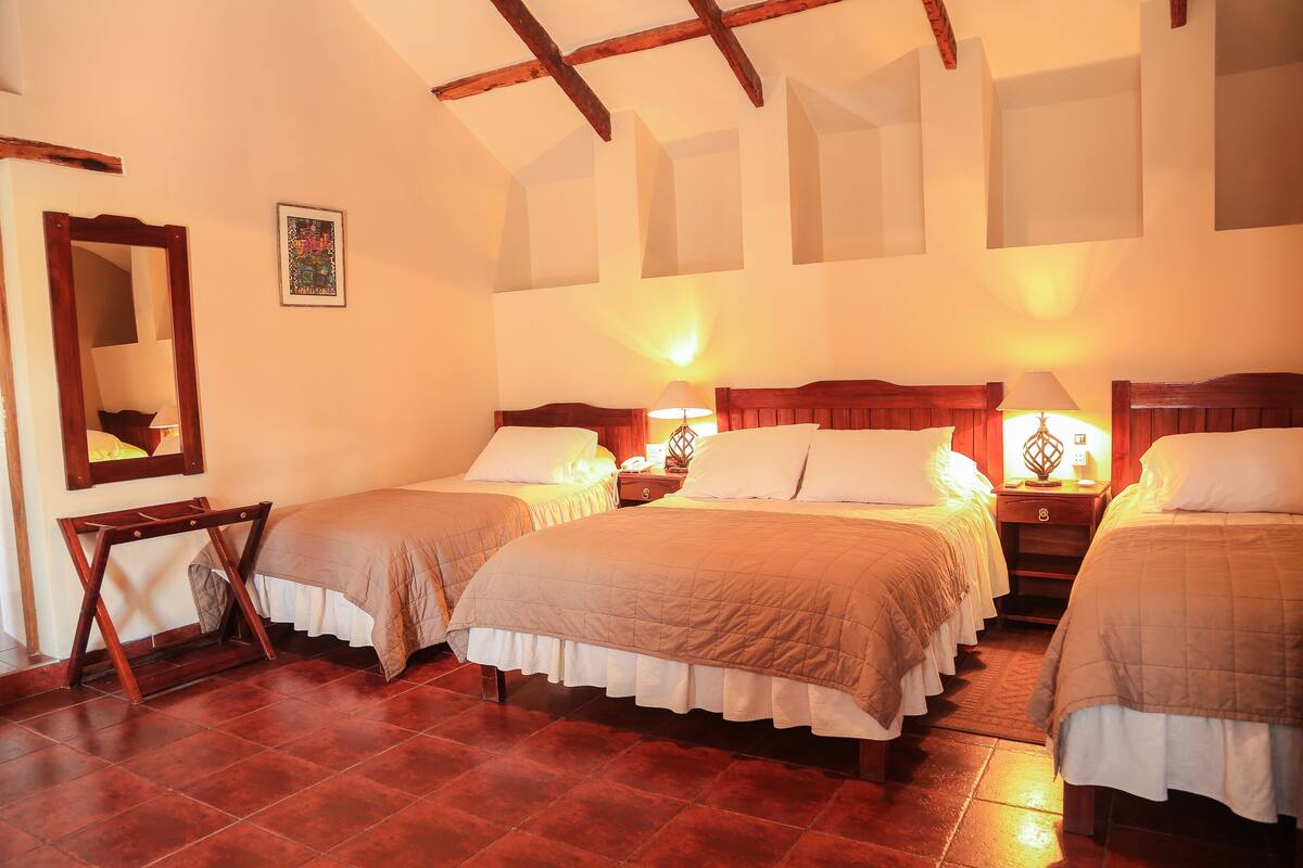 A hotel room with three beds, wooden headboards, and a large mirror.