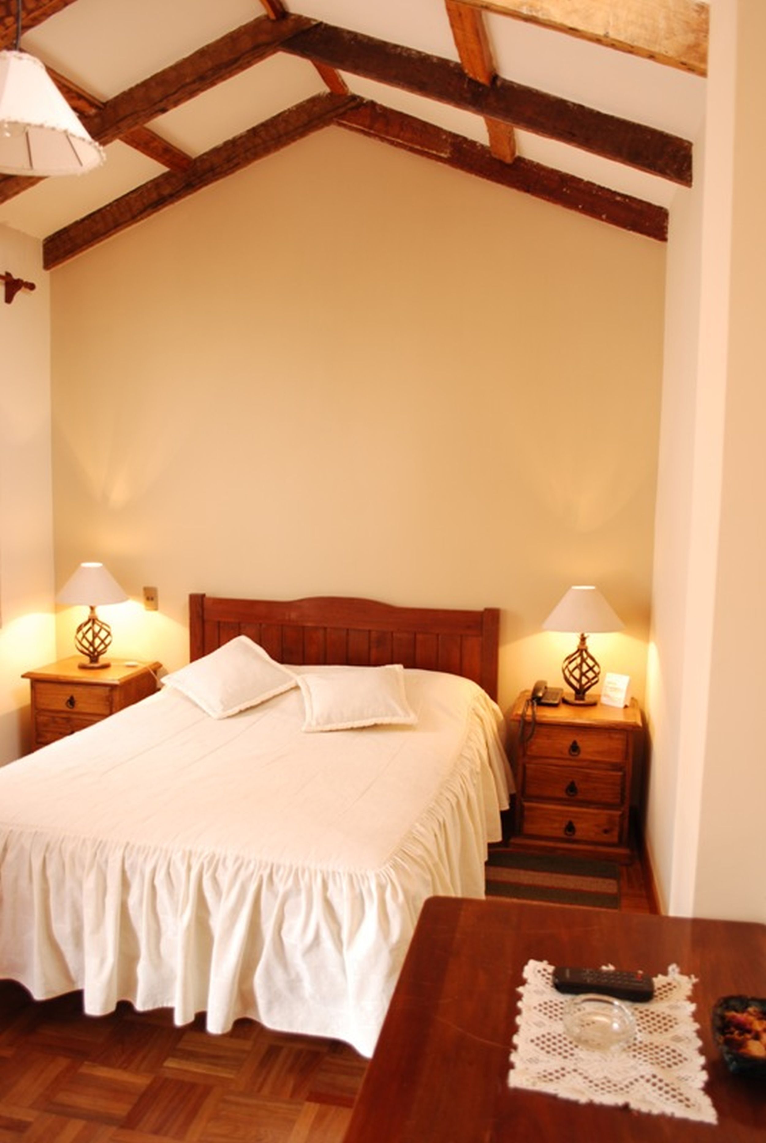 Une chambre à coucher avec un lit en bois, deux tables de chevet avec des lampes, un plancher en bois et une petite table avec une télécommande.