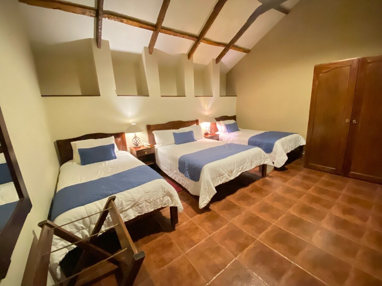 A room with three beds, wooden beams on the ceiling, and a tiled floor.