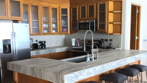 Un'ampia cucina con mobili in legno, una grande isola con sgabelli da bar, elettrodomestici in acciaio inossidabile e un pannello di divisa piastrellato.