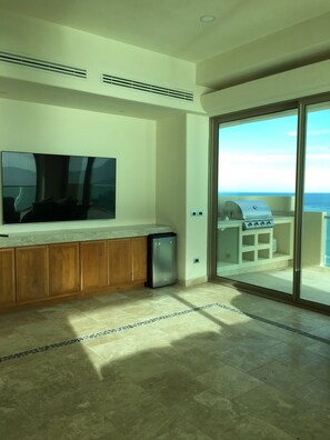 A modern kitchen with a built-in dishwasher, a large flat-screen TV, and a sliding glass door leading to an outdoor grill area.