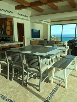 A spacious living area with a large dining table, comfortable seating, and a view of the ocean.