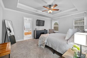 A bedroom with a bed, a TV, a ceiling fan, and a window.