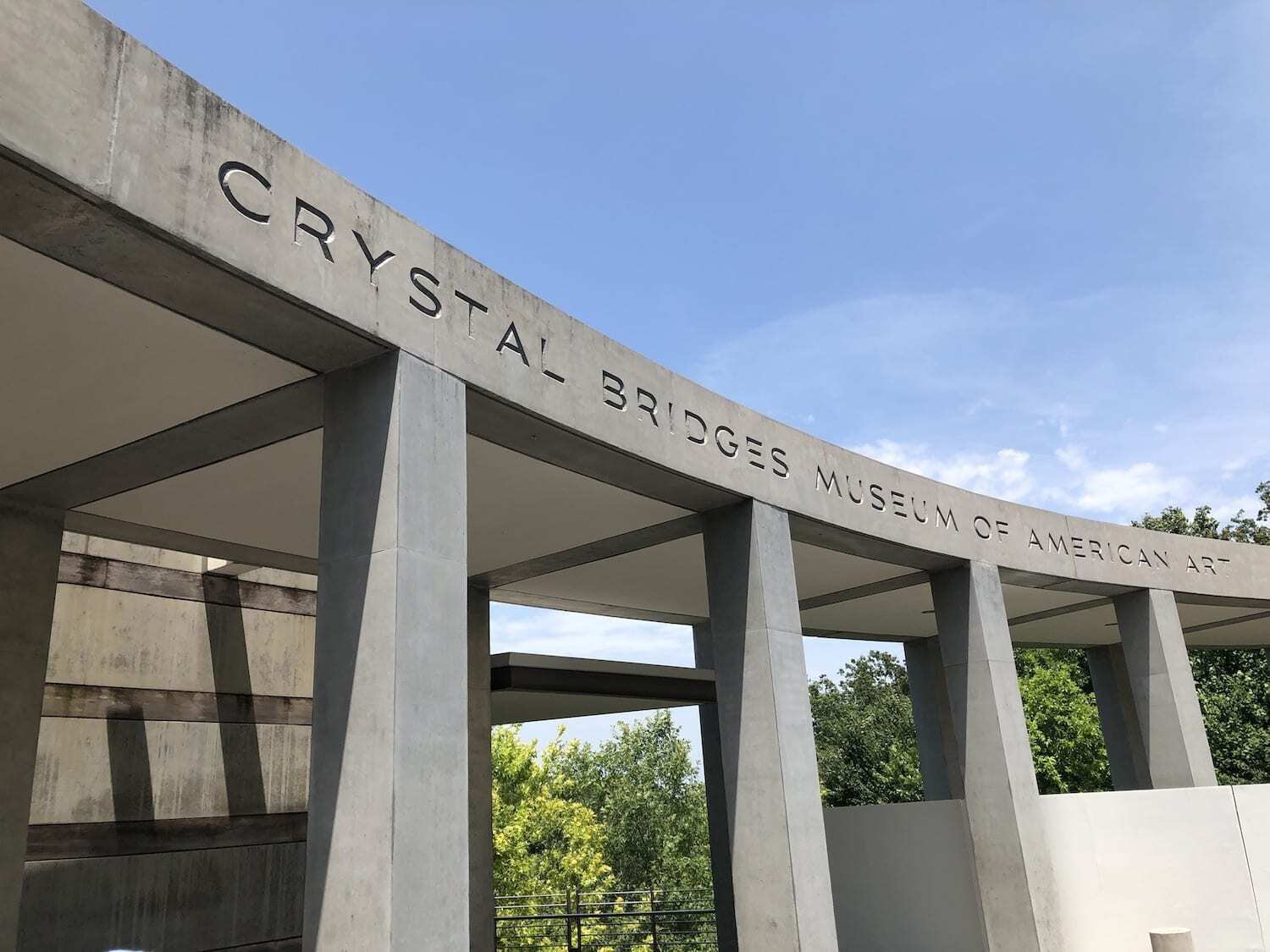 Ingången till Crystal Bridges Museum of American Art, med en klar himmel och träd i bakgrunden.