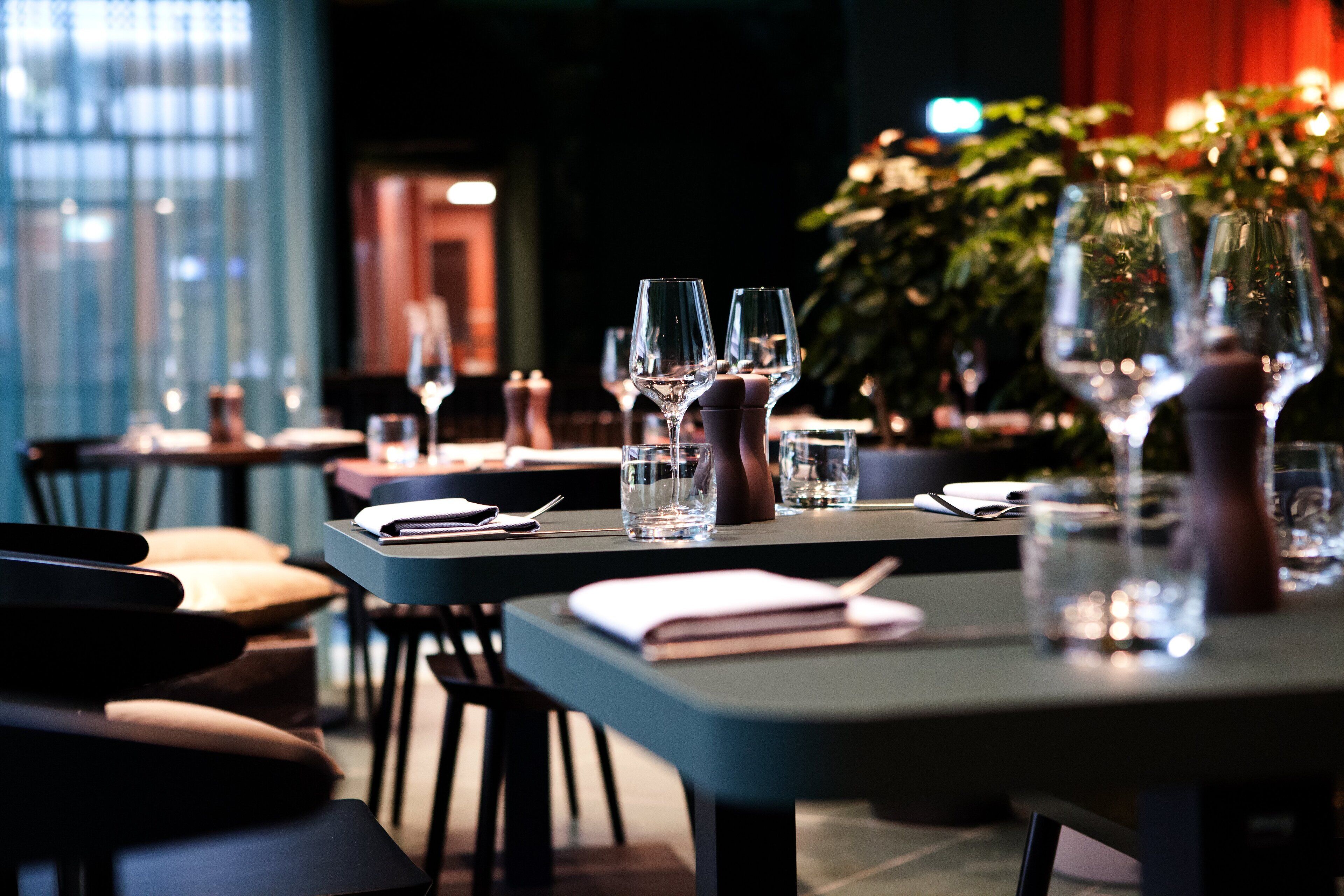 Een restaurantsetting met gedekte tafels, helder glaswerk en een notitieboekje op tafel.