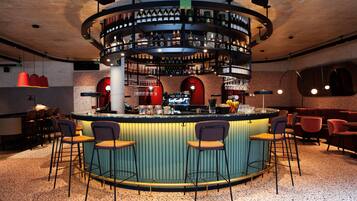 Zona de bar con una barra circular, varios taburetes y una estantería para vinos.