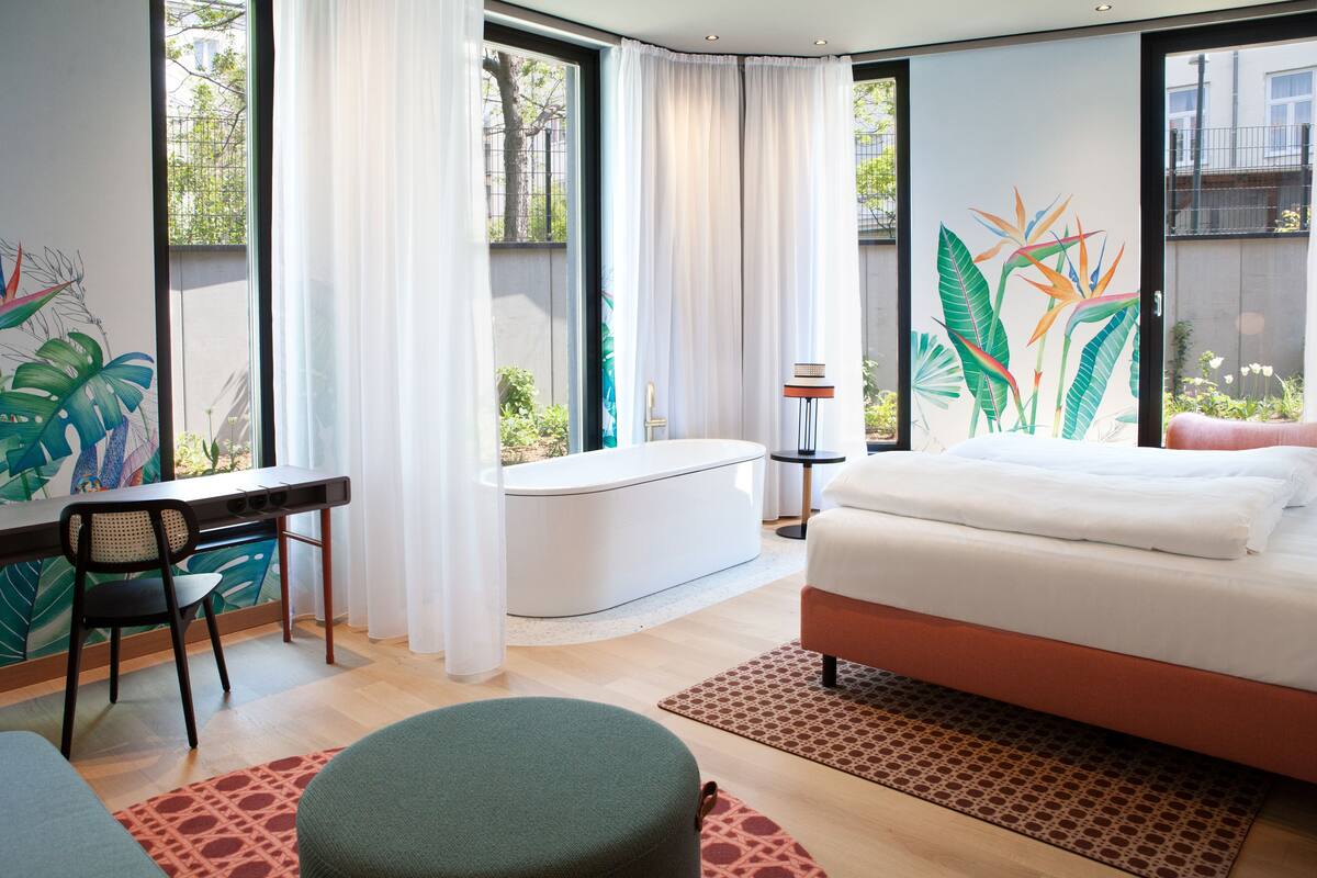 A modern bedroom with a bed, a desk, and a bathtub.