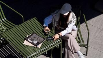 A person sitting on a green metal bench with a laptop, a cup, and a spoon.