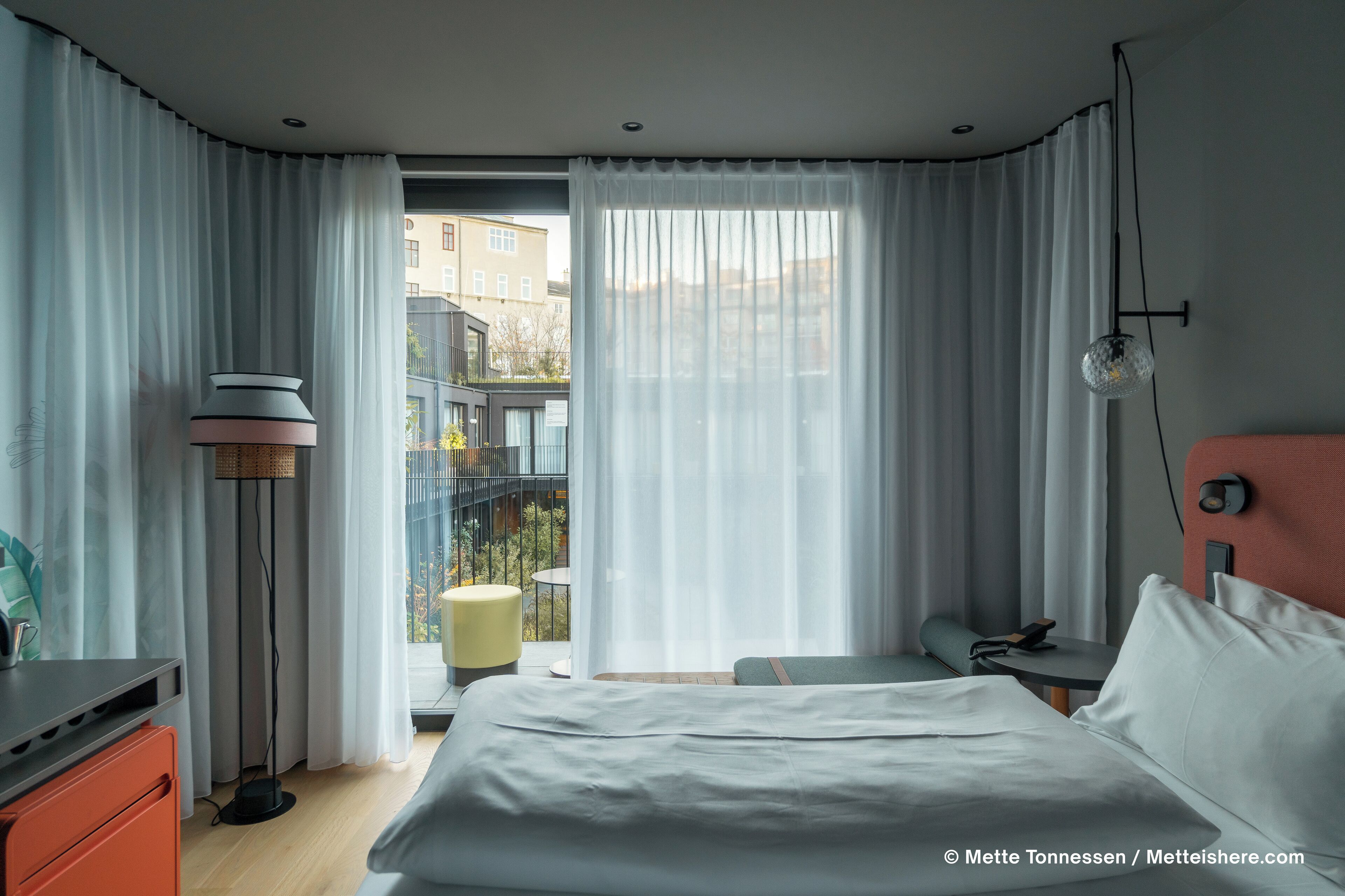 A hotel room with a bed, a desk, a lamp, and a view of the outside.