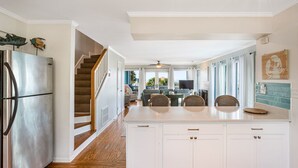Una cocina amplia con armarios blancos, un refrigerador de acero inoxidable y una escalera de madera que conduce a un comedor.