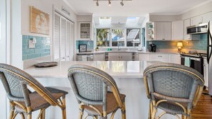 Una cocina moderna con una isla central, sillas de mimbre y vistas al exterior.