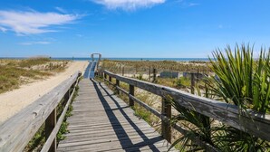 Un paseo marítimo de madera que conduce a una playa con dunas y un cielo despejado.