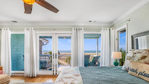 Un dormitorio con una cama grande, vistas a la playa y un balcón con sillas.
