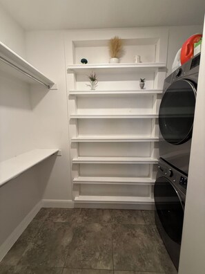 A laundry room with a built-in washer and dryer, white shelving units, and a small decorative plant. - Modern and cozy three bedroom townhome (Hurricane)