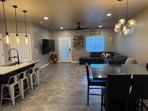 A modern kitchen with a central island, dining area with chairs, and a living room with a sofa and a TV.