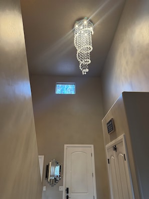 A hallway with a chandelier, a small window, and a door.