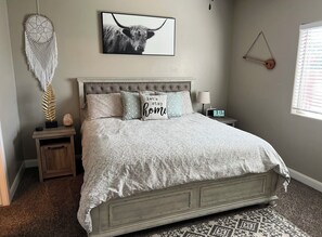 A bedroom with a bed, a nightstand, a wall clock, a dreamcatcher, and a framed picture.