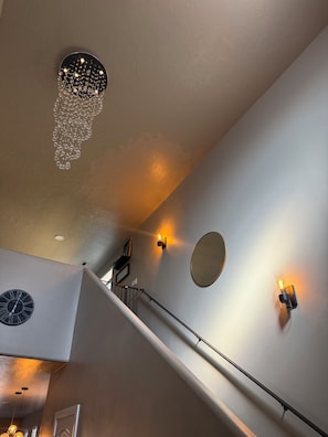 A staircase with a handrail, a wall-mounted clock, and a light fixture with a circular mirror. - Modern and cozy three bedroom townhome (Hurricane)