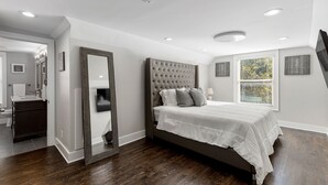 Un dormitorio con una cama grande, un espejo, una ventana con persianas y un suelo de madera oscura.