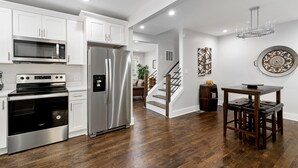 Una cocina moderna con electrodomésticos de acero inoxidable, una mesa de comedor de madera y una escalera que sube a otro nivel.