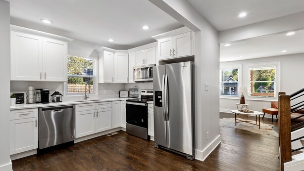 Una cocina moderna con armarios blancos, electrodomésticos de acero inoxidable y piso de madera.