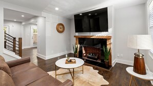 Una sala de estar moderna con chimenea, televisor de pantalla plana y una escalera que sube a otro nivel.
