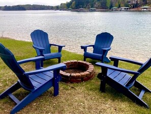 A lakeside setting with two Adirondack chairs facing a fire pit.