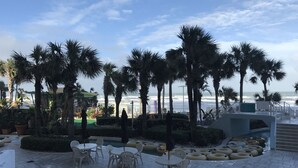 A terrace with outdoor seating, palm trees, and a view of the ocean.