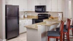 Una cocina con gabinetes blancos, un refrigerador negro, un microondas, una estufa y encimeras de granito.