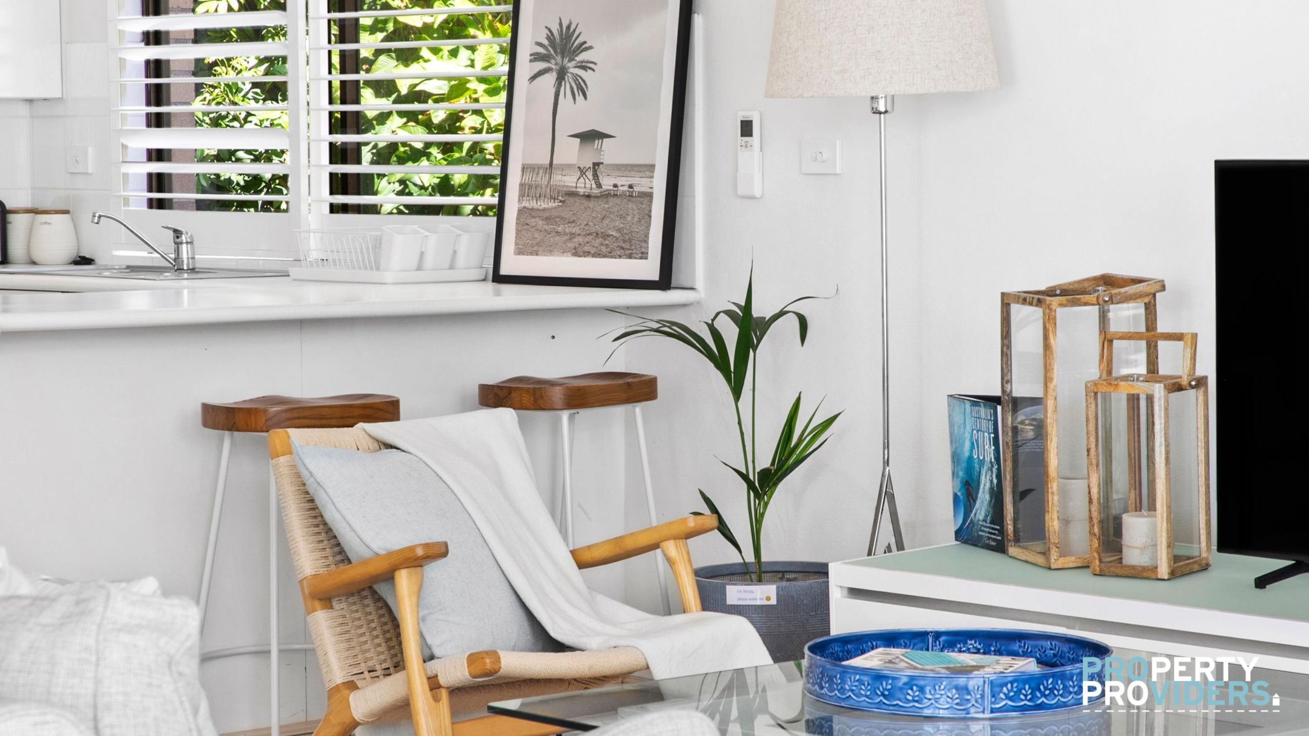 A modern living room with a sofa, a chair, a small table, a lamp, a framed picture, a potted plant, and a decorative shelf with glass containers.
