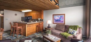 A cozy living area with a kitchen, wooden furniture, a sofa, a coffee table, and a painting on the wall. - Iron Blosam Week 50 (Sandy)