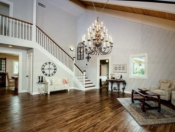 A spacious loft with a high ceiling, a grand chandelier, a staircase, and a cozy seating area.