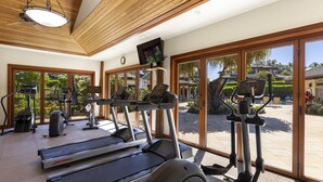 A gym with treadmills, elliptical machines, and a television on the wall.
