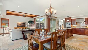 A spacious kitchen with wooden cabinets, a dining area with a glass-top table, and a large chandelier.