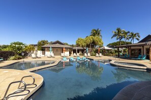 Ein Swimmingpool mit LiegestĂŒhlen und Sonnenschirmen, umgeben von Palmen und wolkenlosem, blauem Himmel.
