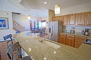 A kitchen with granite countertops, wooden cabinets, a stainless steel refrigerator, a toaster, and a blender.