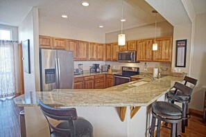 A kitchen with wooden cabinets, stainless steel appliances, a granite countertop, and bar stools.