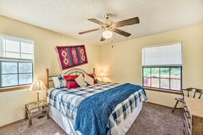 A bedroom with a bed, a ceiling fan, a window with blinds, a nightstand with a lamp, and a wall hanging. - Quiet Ruidoso Getaway ~ 18 Mi to Ski Apache! (Ruidoso)