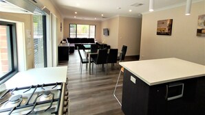A modern kitchen with a gas stove, dining area with chairs, and a living space with a sofa. - New, Modern Property built in 2021 * Close to Town (Glenroy)