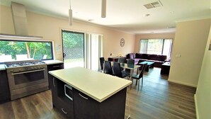A modern kitchen with a central island, dining area with chairs, and a living room with a sofa. - New, Modern Property built in 2021 * Close to Town (Glenroy)