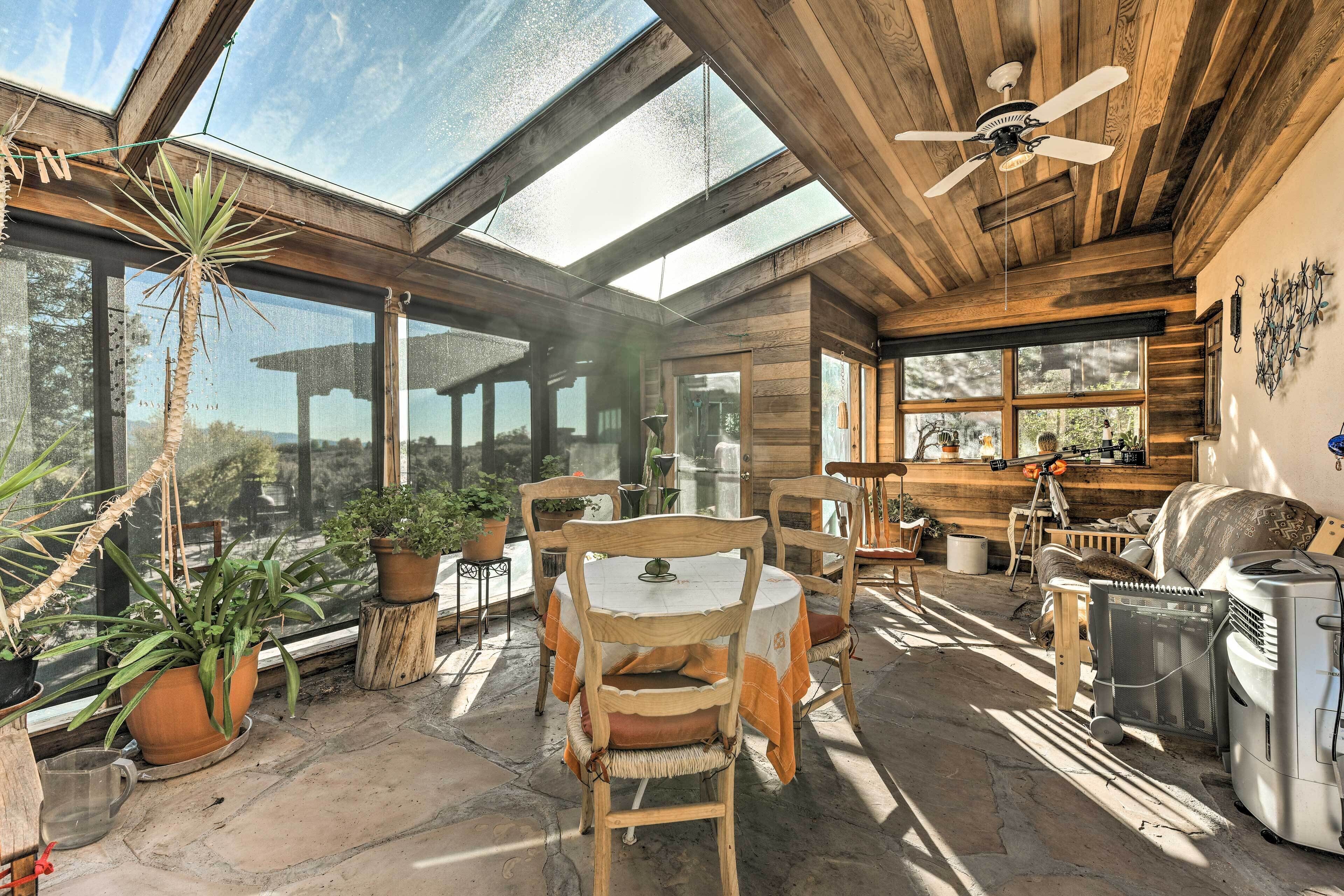 Een zonnig terras met houten meubels, planten in potten en een plafondventilator.
